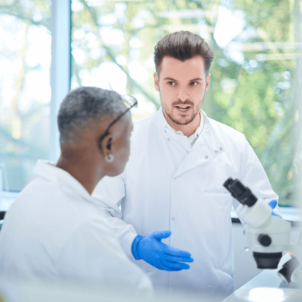 Two medical professionals having a conversation over a microscope.